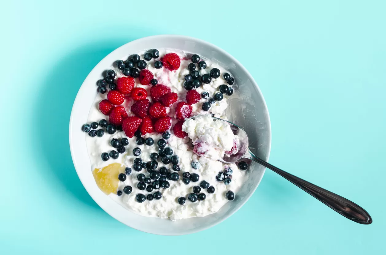 A spoon in a plate with cottage cheese and sour cream on a blue background. Healthy food berries and cottage cheese in a plate