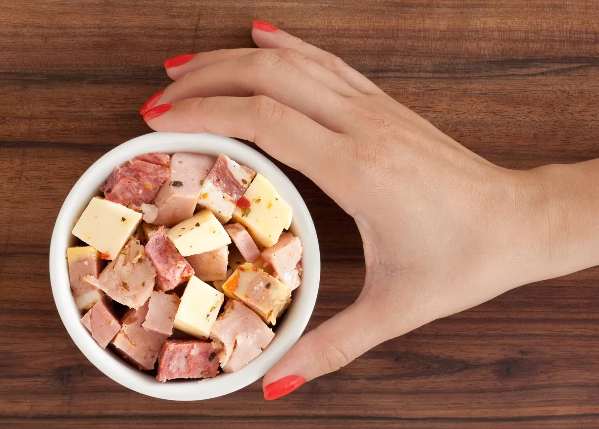 Woman hand holding bowl full of diced cheese and cured meats