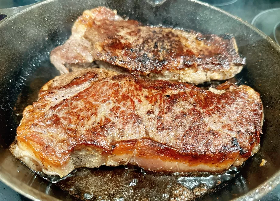 steaks cooking in a cast iron skillet