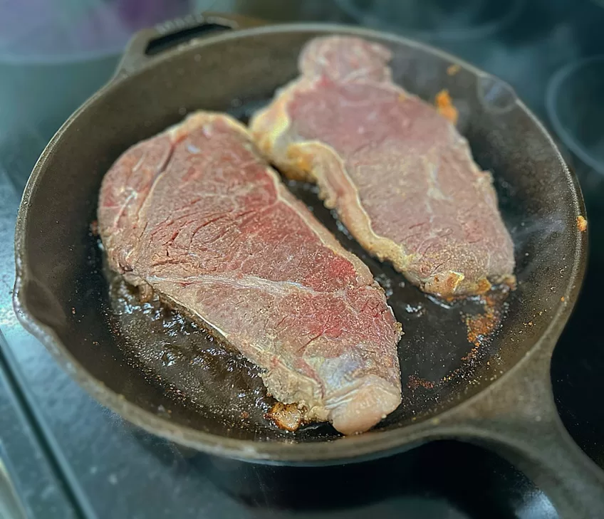 steaks cooking in a cast iron skillet