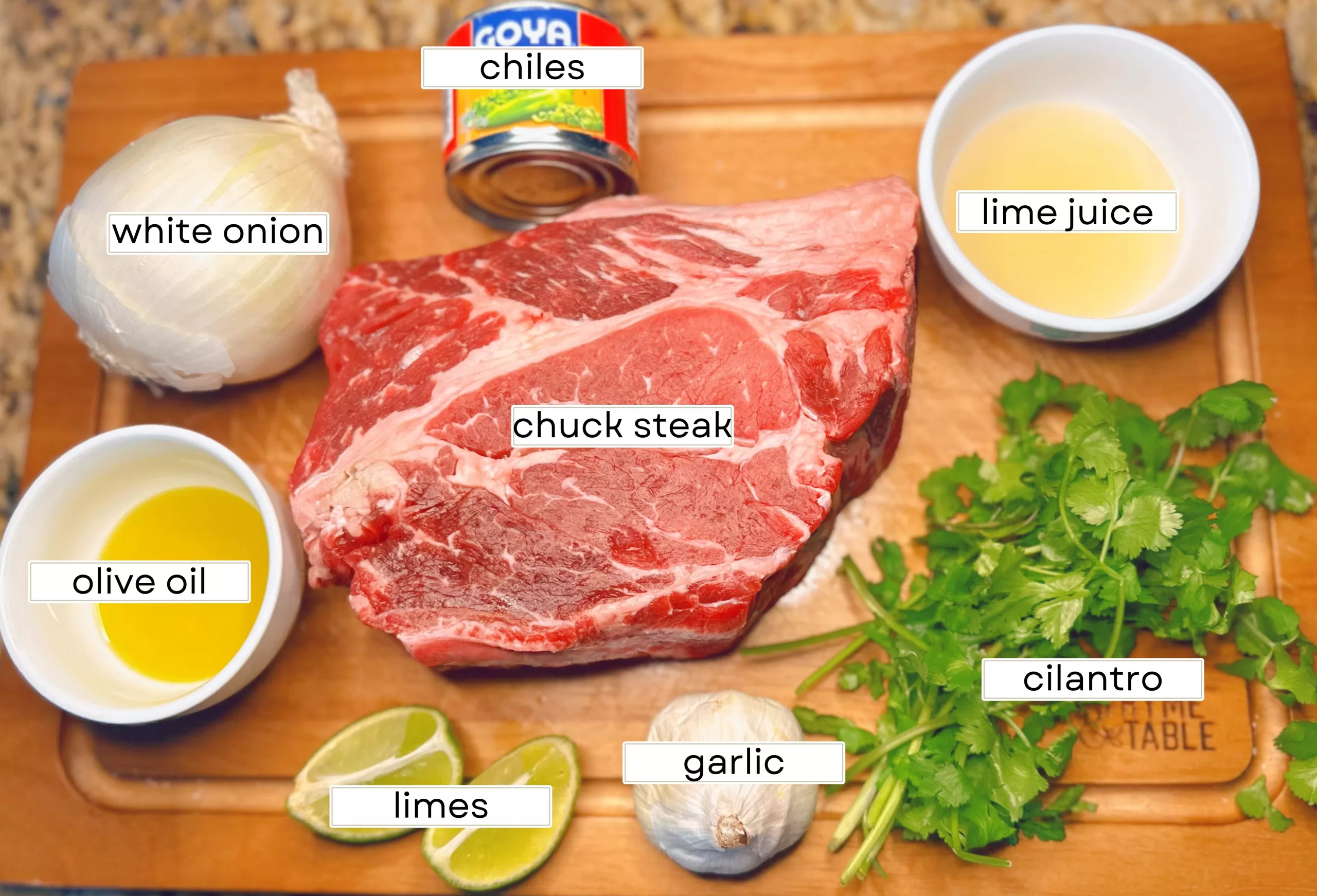 cutting board with chuck roast, cilantro, garlic, lime, chiles, onion, olive oil, and lime juice