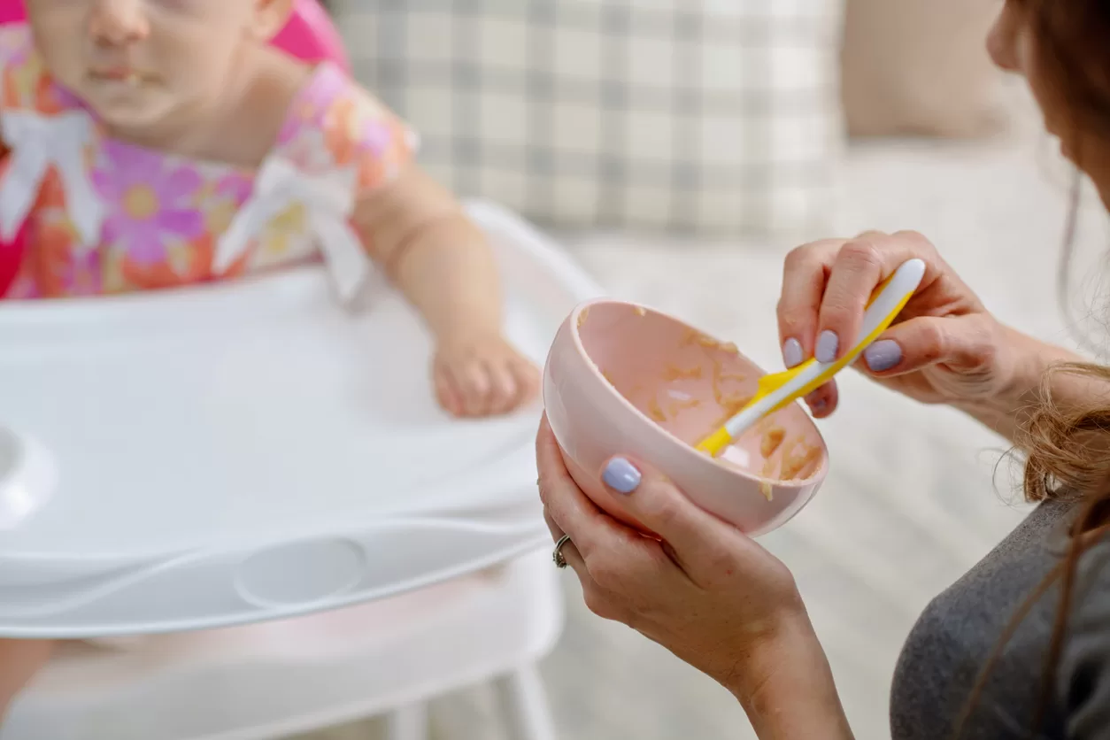 Closeup image of mother giving spoon of food to baby girl