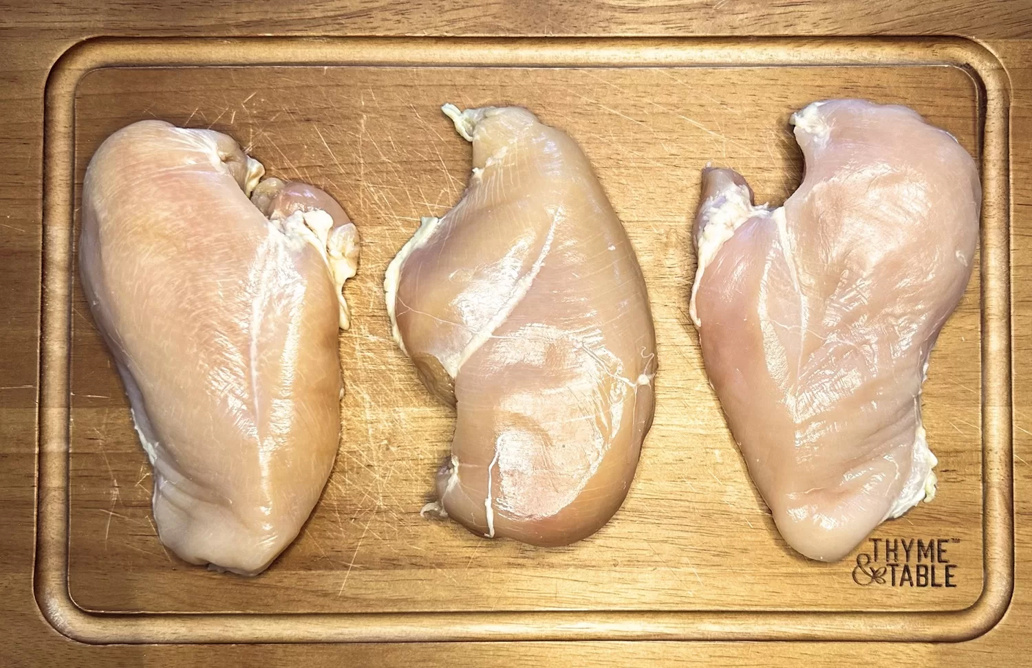 3 raw chicken breasts on a wooden cutting board