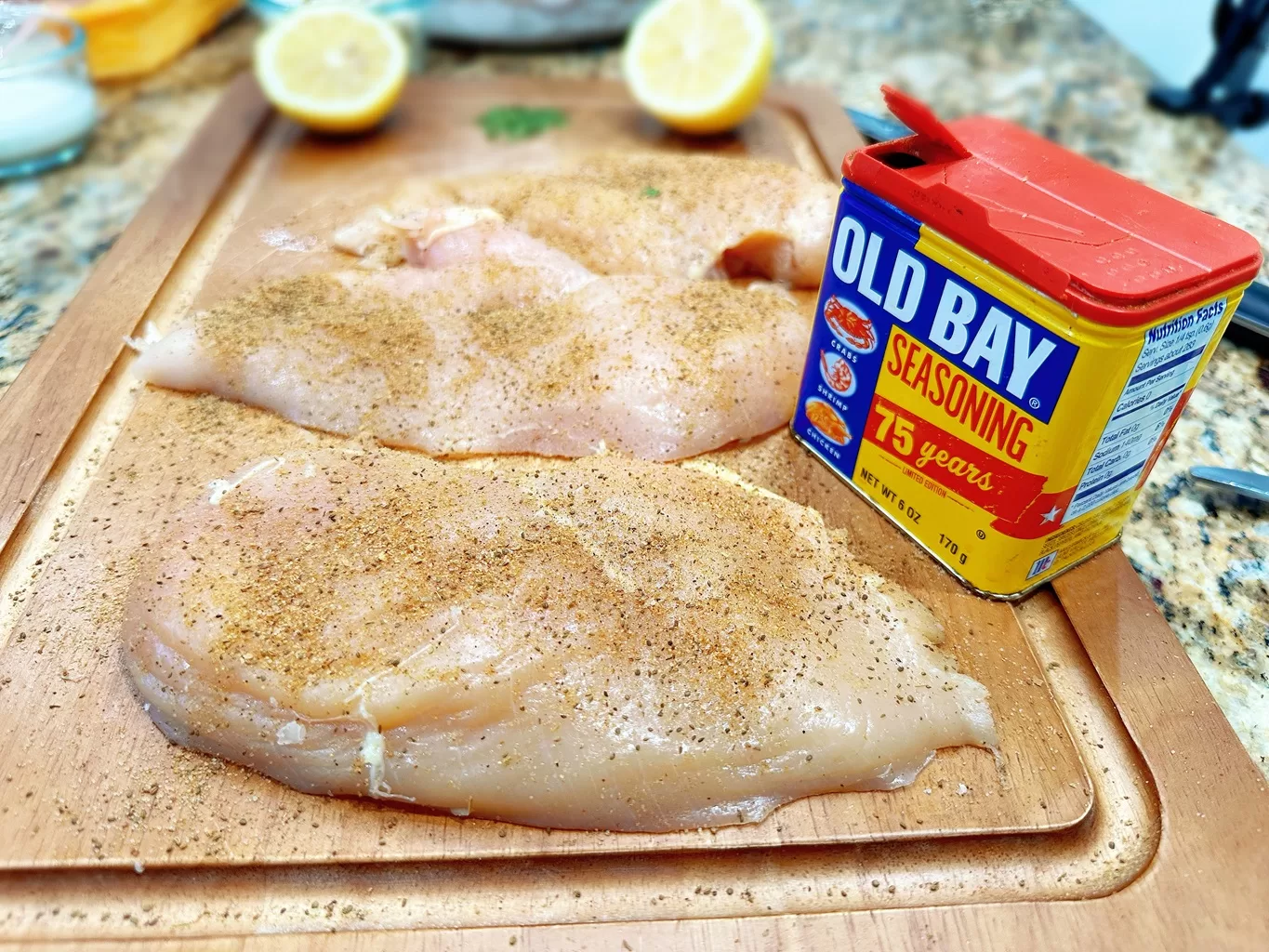 raw chicken breast with old bay seasoning on cutting board