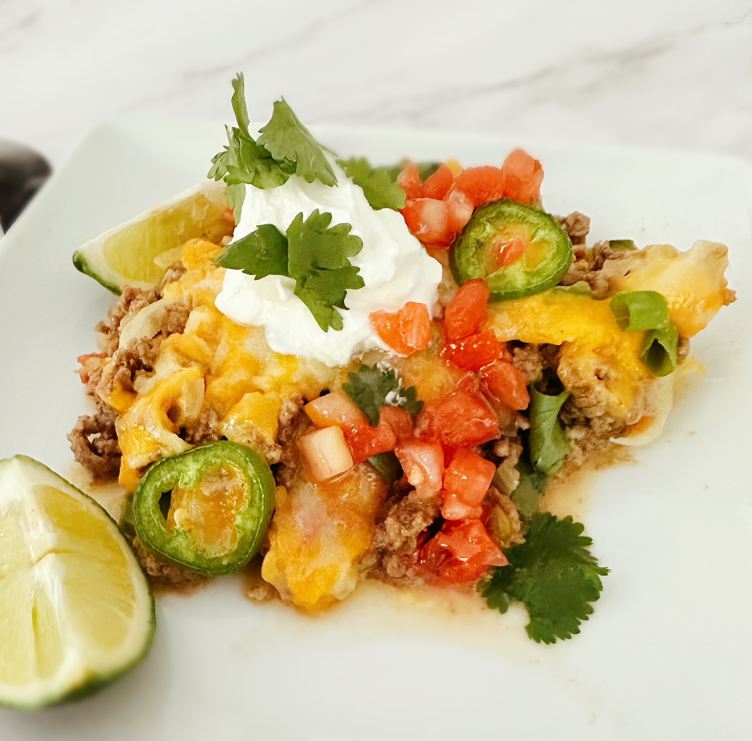 keto mexican taco casserole on a white dish with fresh lime, sour cream, and cilantro