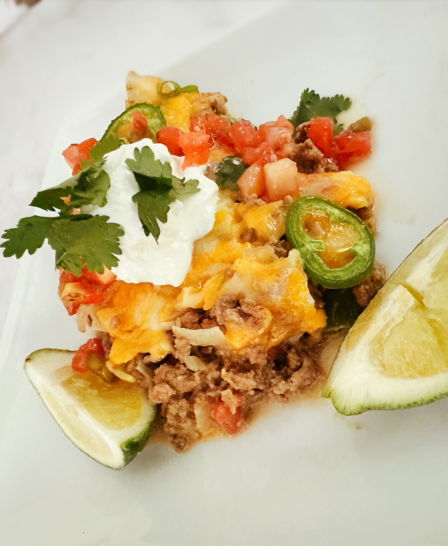 keto mexican taco casserole on a white dish with fresh lime, sour cream, and cilantro