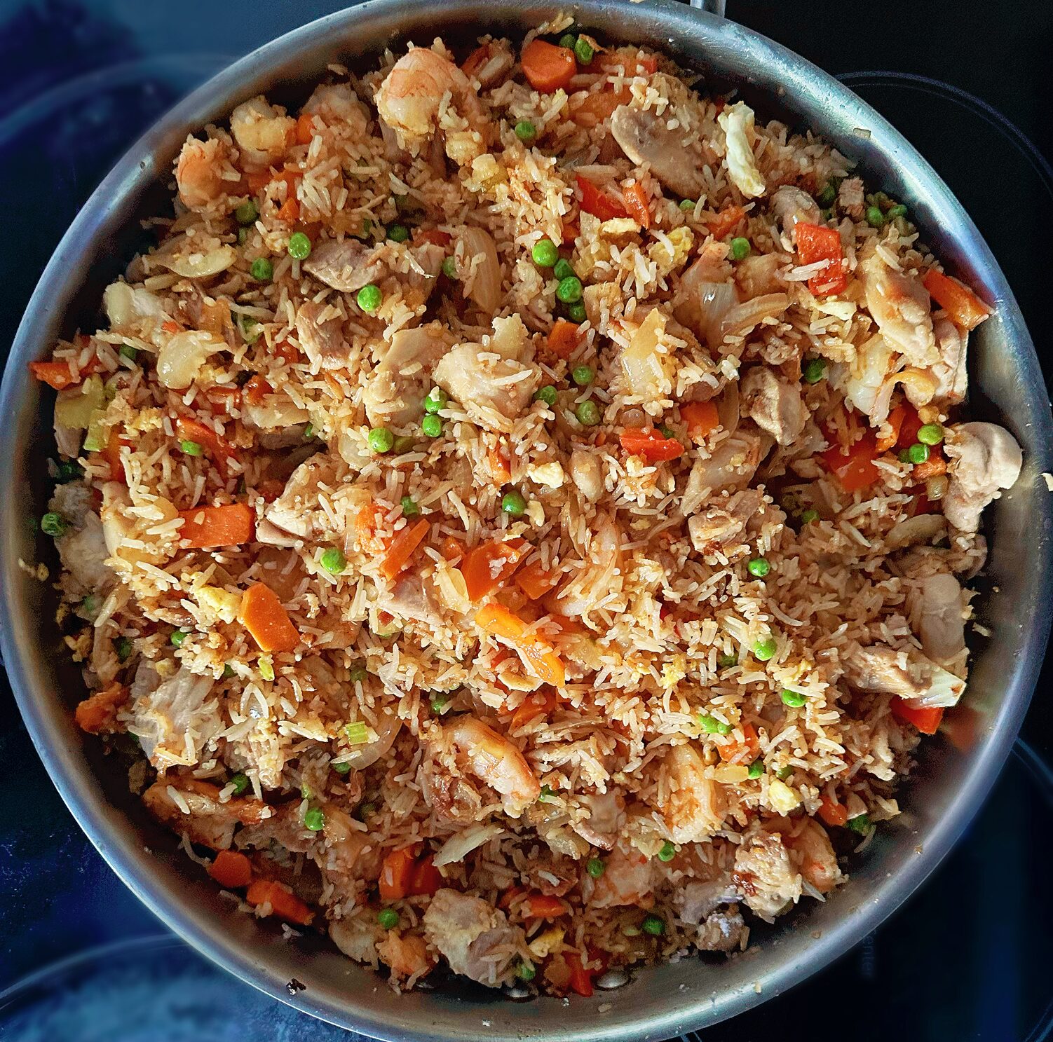 carrots, peas, onions, scrambled eggs, chicken, shrimp and rice frying in a pan