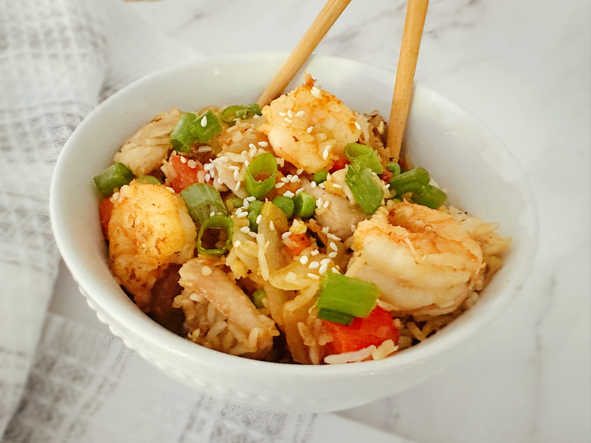 chinese chicken and shrimp stir fry in a white bowl with wooden chopsticks in the bowl and a kitchen rag in the background