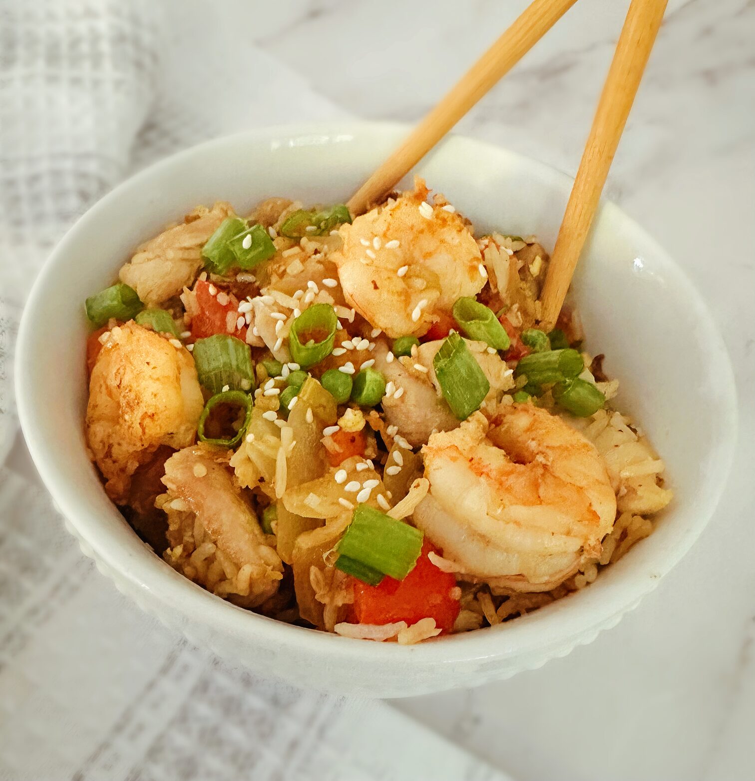 chinese chicken and shrimp stir fry in a white bowl with wooden chopsticks in the bowl and a kitchen rag in the background