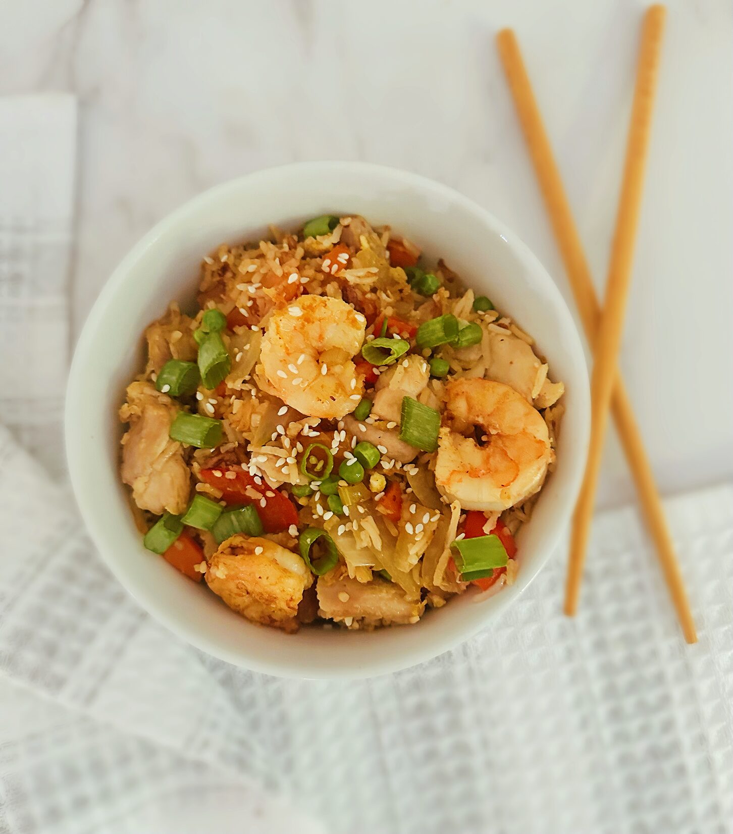 chinese chicken and shrimp stir fry in a white bowl with wooden chopsticks next to in and a kitchen rag in the background