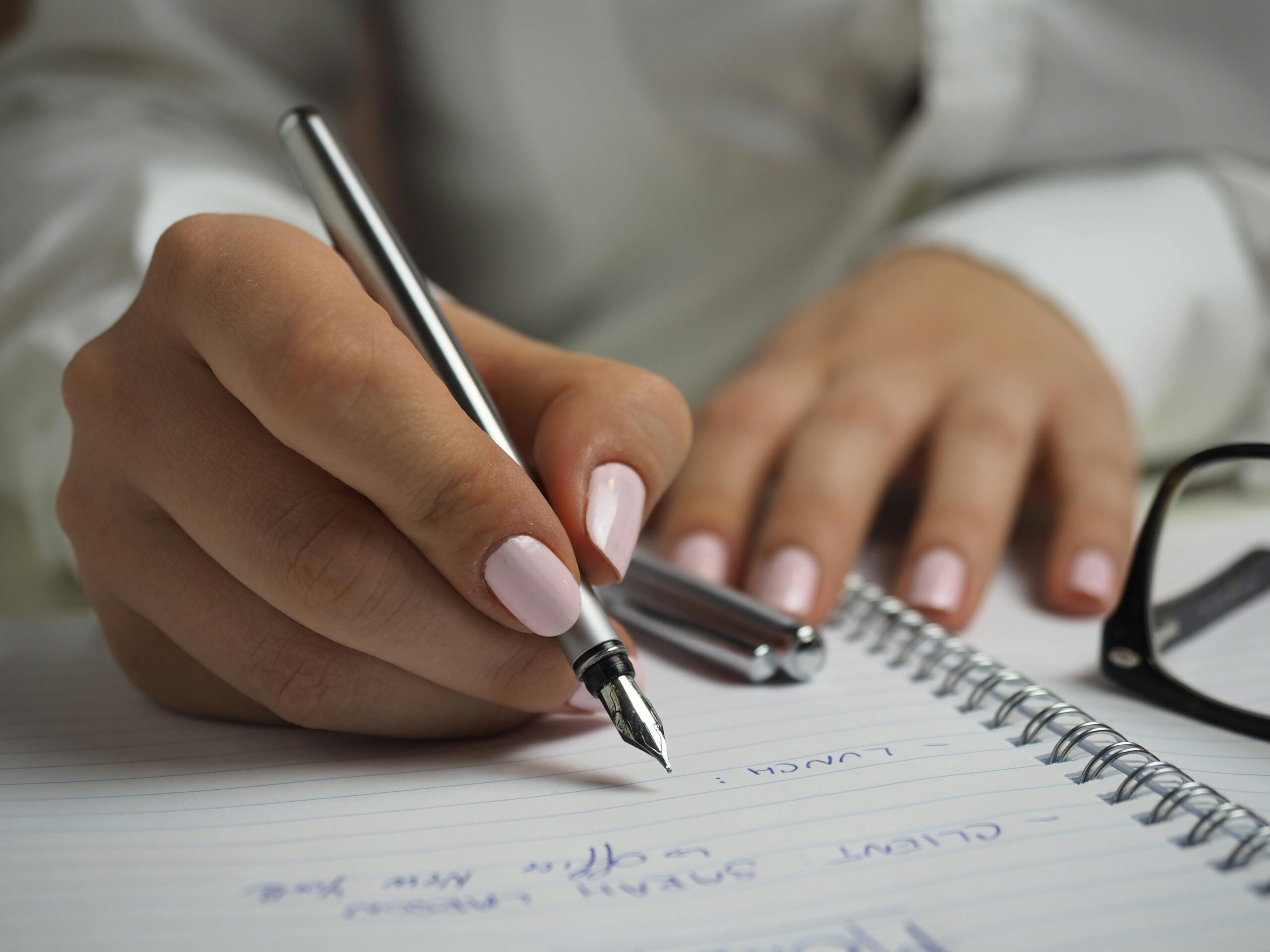 woman with painted nails holding a pen writing in a notebook