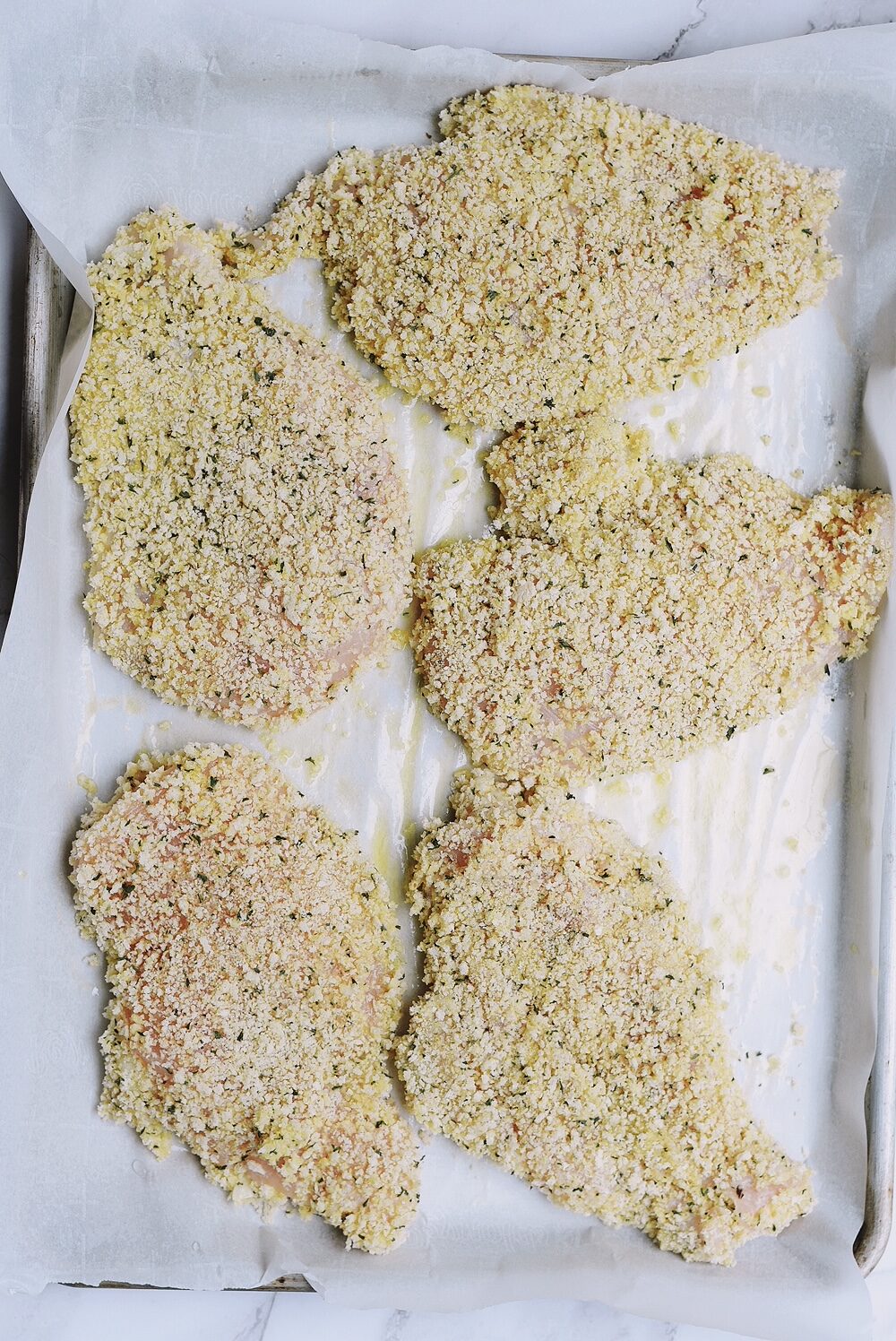 chicken breasts breaded with panko breadcrumbs on a baking sheet with parchment paper