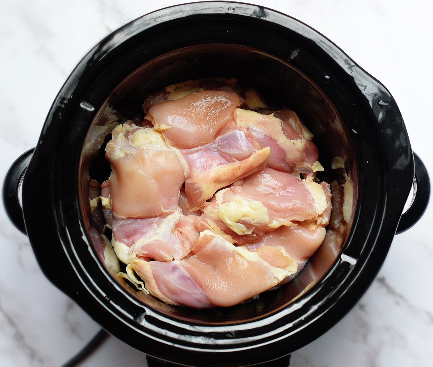 raw chicken cooking inside of a crock pot