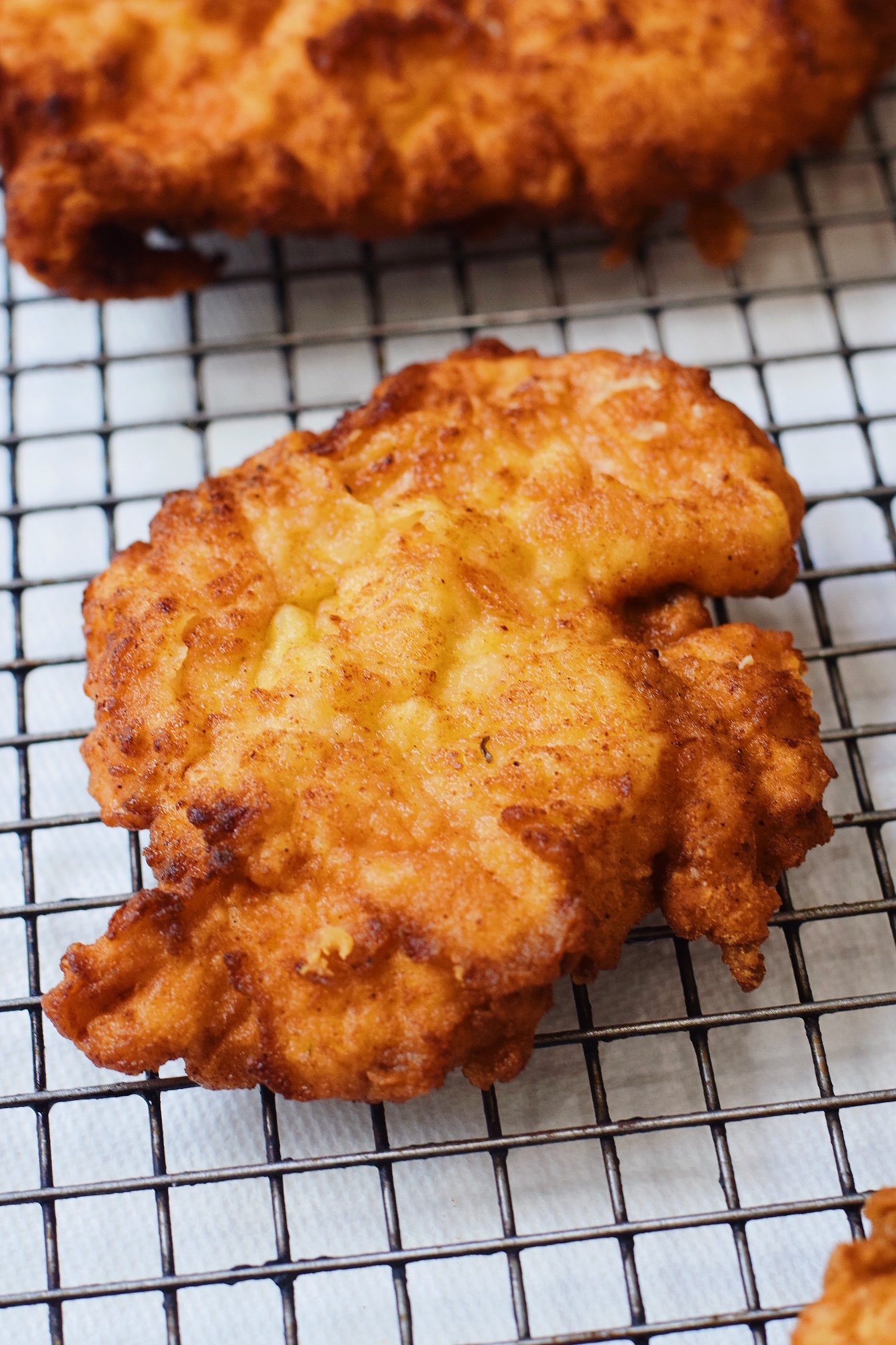 closeup of juicy, golden brown fried chicken on a wire rack cooling