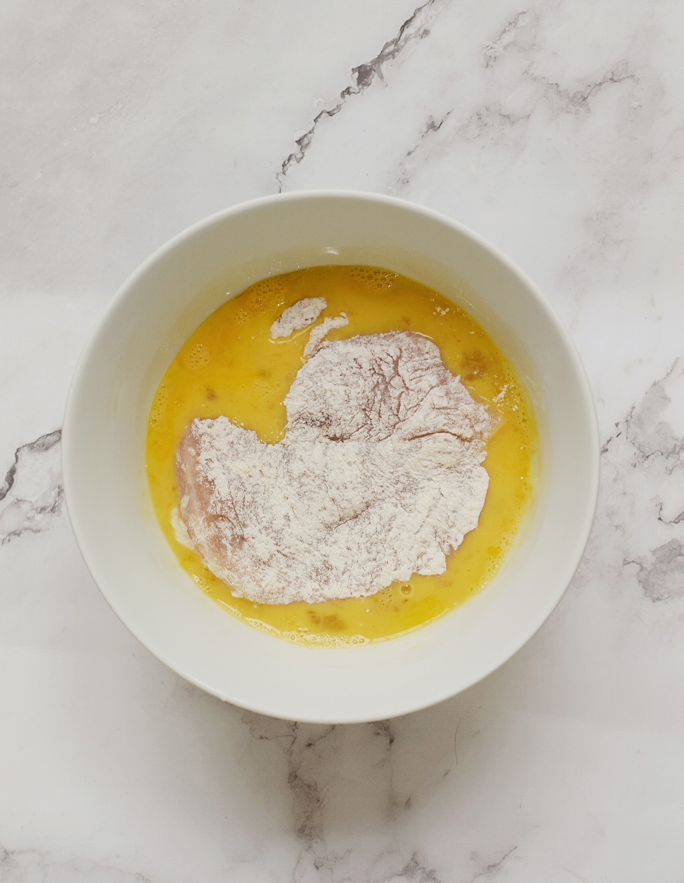 floured chicken submerged in a bowl of eggs