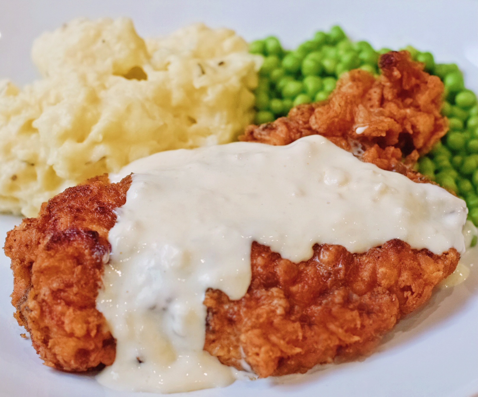 chicken fried chicken with country gravy on a plate with peas and mashed potatoes