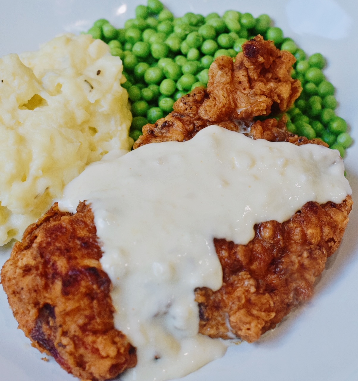 chicken fried chicken with country gravy on a plate with peas and mashed potatoes