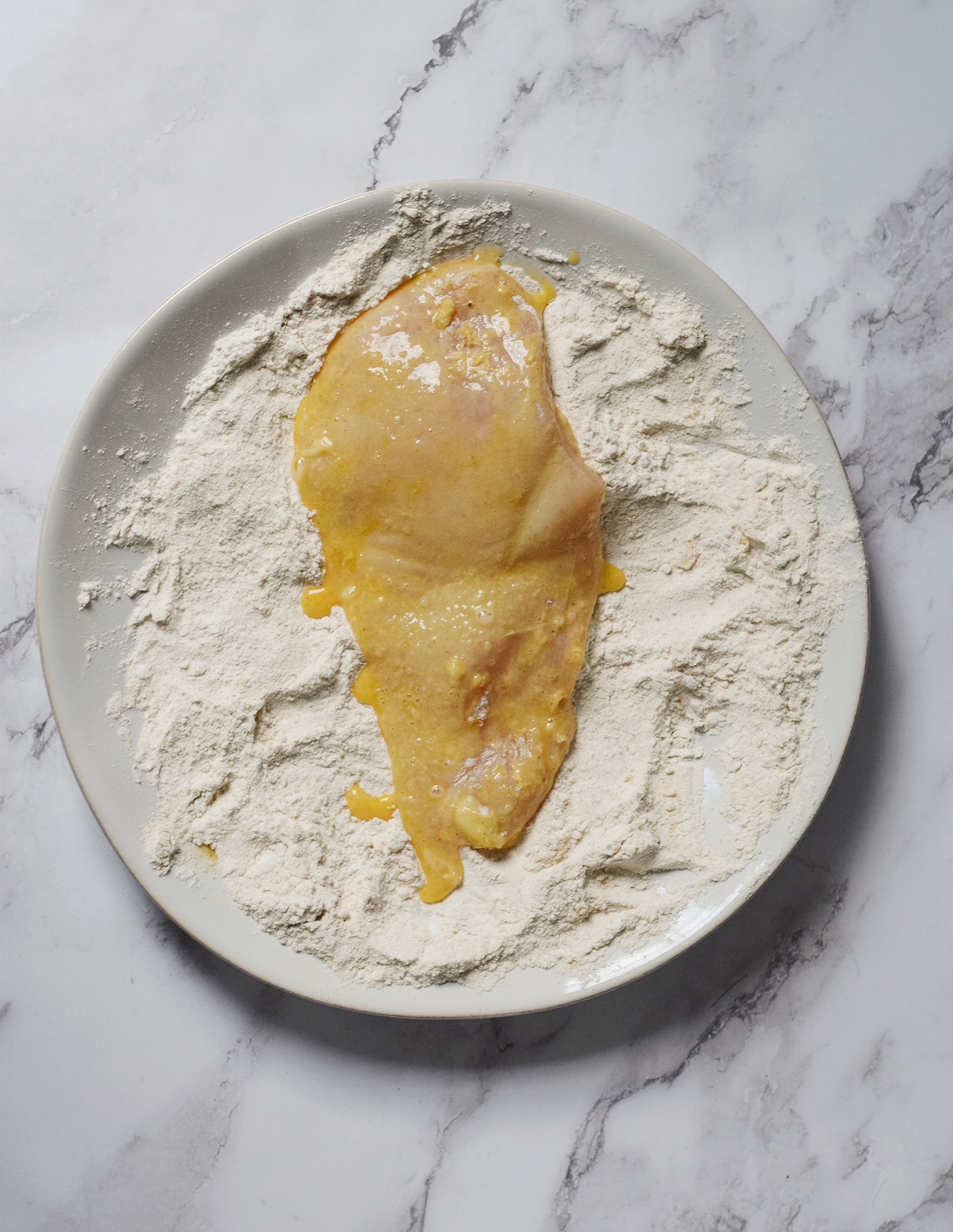 chicken coated in egg mixture being dredged in flour mixture