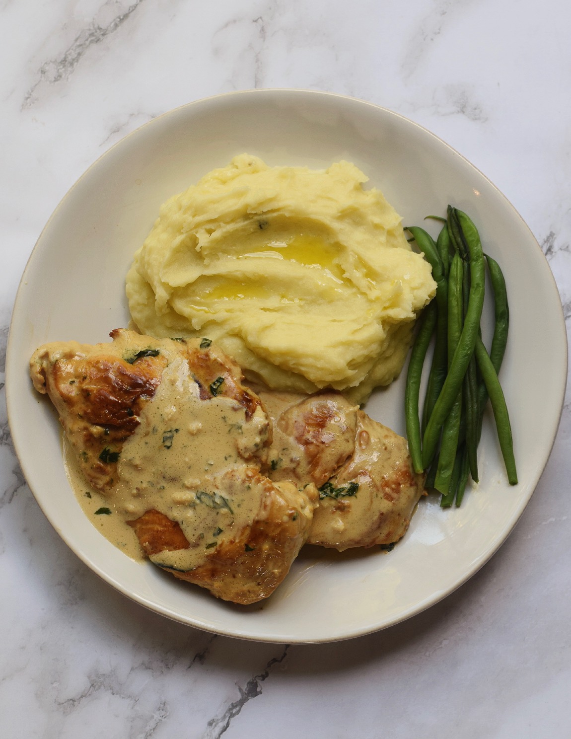 Garlic Herb Boursin Chicken on a white dinner plate with green beans and mashed potatoes