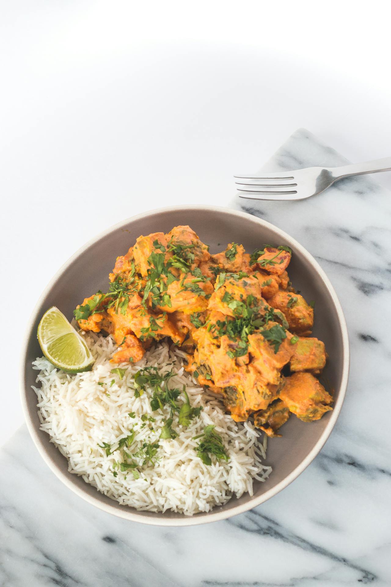 indian butter chicken with rice and lime in a white bowl on a white marble counter