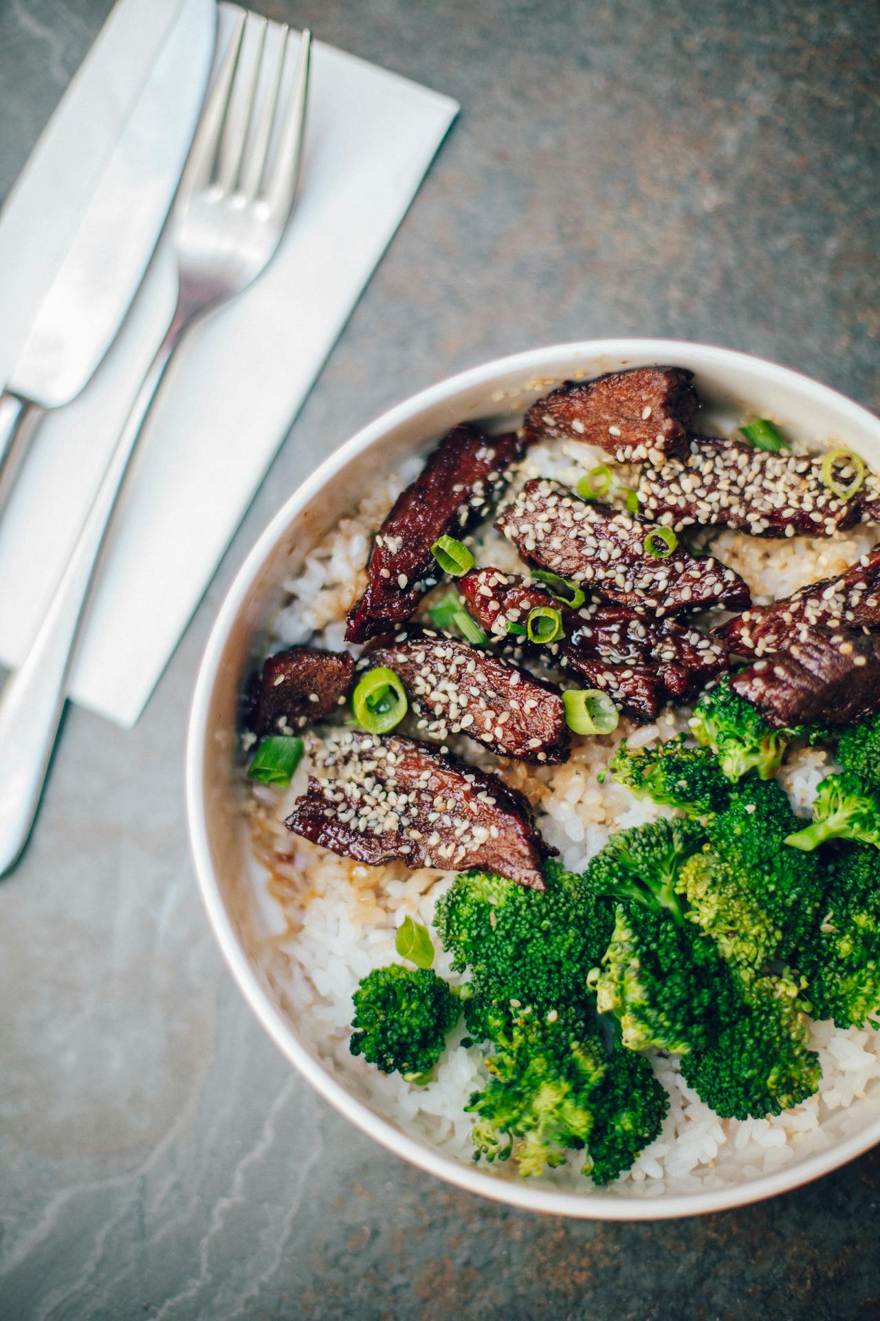 chinese beef and broccoli in a white bowl topped with sesame seeds