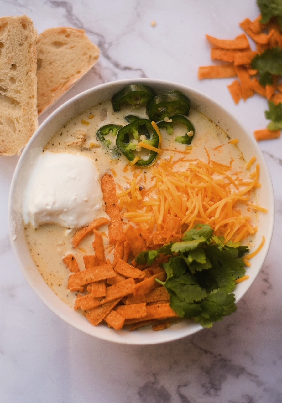 creamy white chicken chili recipe in a white bowl with fresh bread and tortilla strips in the background