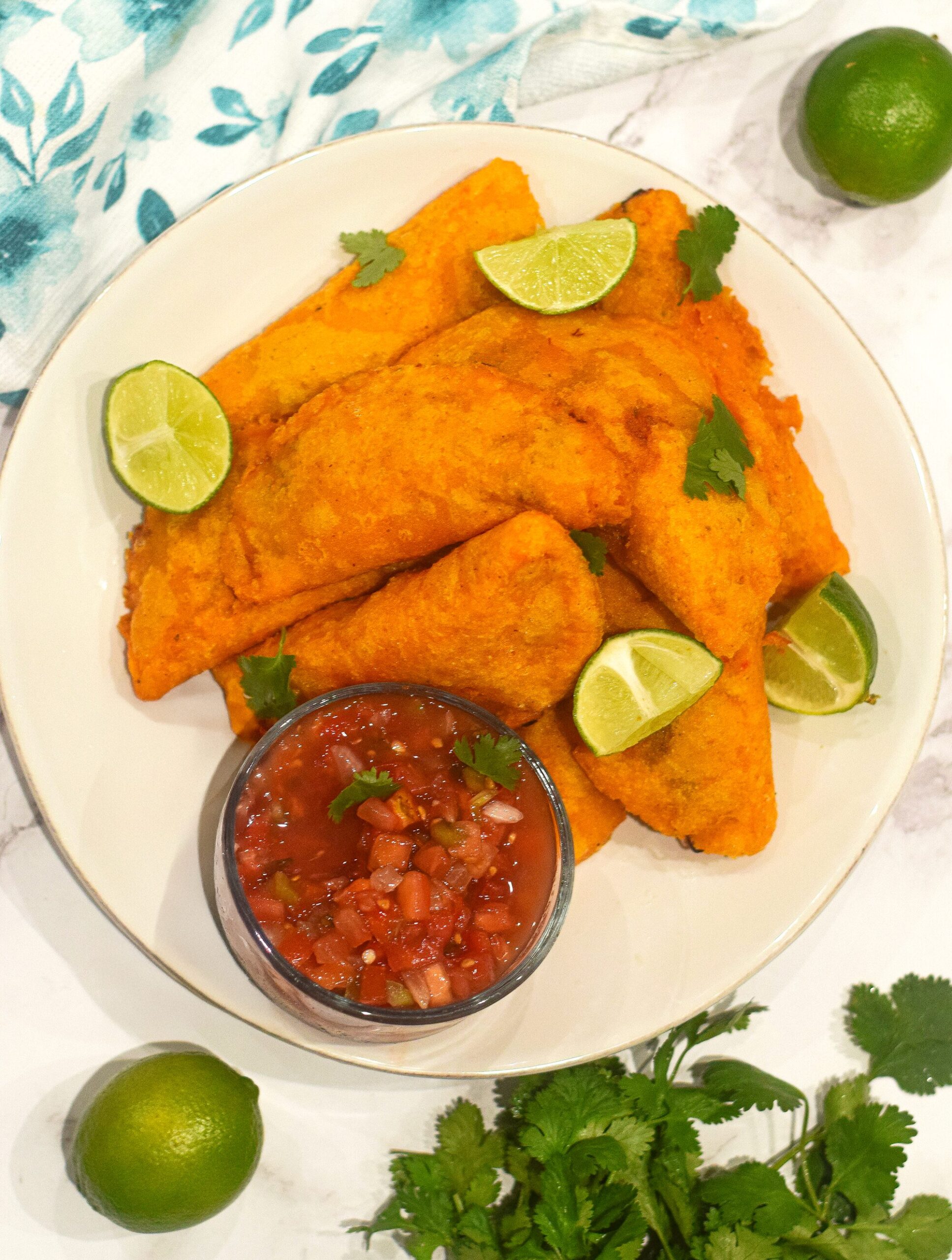 colombian empanadas on a white plate with salsa, limes and fresh cilantro