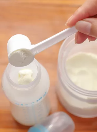 womans hand putting formula into bottle