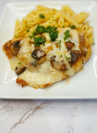 smothered chicken breast topped with melted cheese and onions served with pasta