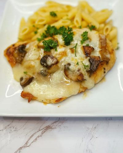 smothered chicken breast topped with melted cheese and onions served with pasta