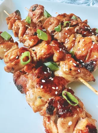 chinese chicken on bamboo skewers topped with sesame seeds and green onion