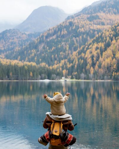 baby on dads shoulders in front of a lake with mountains in the background