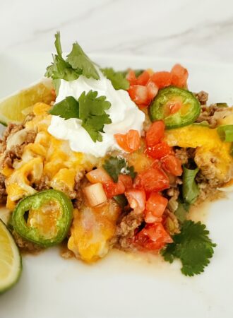 keto mexican taco casserole on a white dish with fresh lime, sour cream, and cilantro