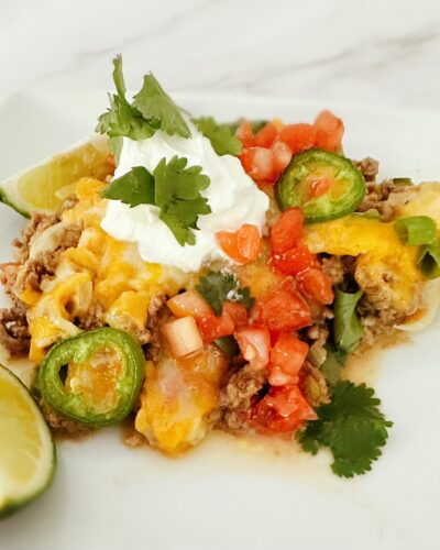 keto mexican taco casserole on a white dish with fresh lime, sour cream, and cilantro