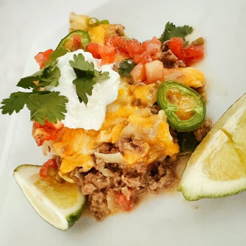 keto mexican taco casserole on a white dish with fresh lime, sour cream, and cilantro