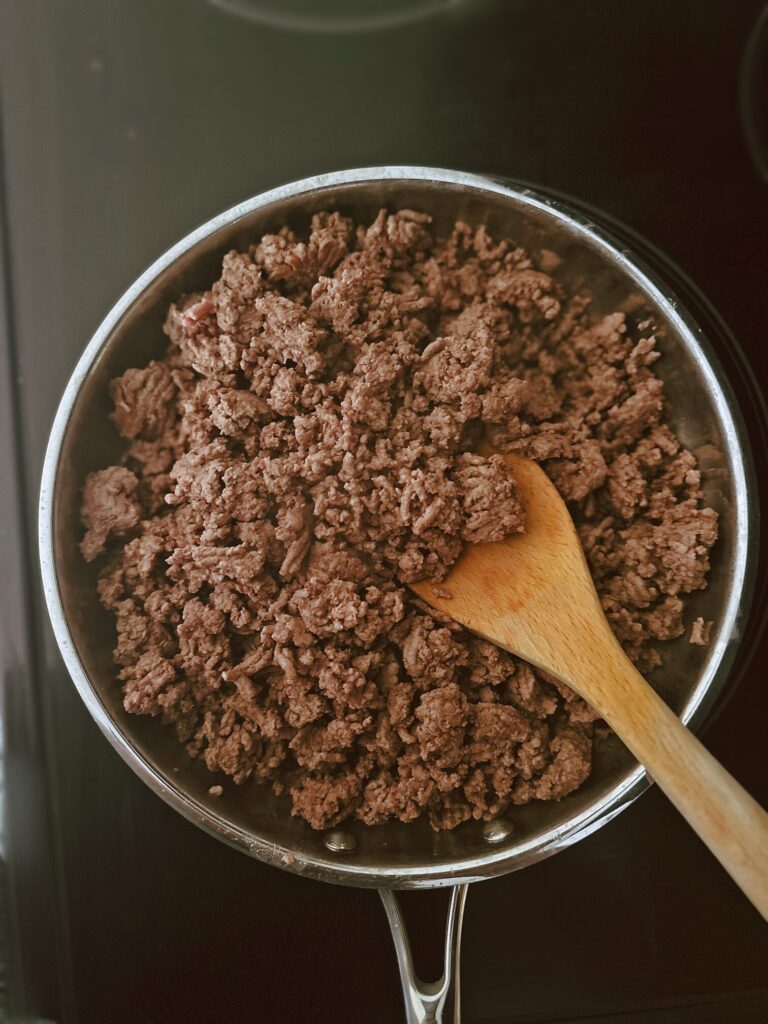 ground beef taco meat cooking in a frying pan with a wooden spoon