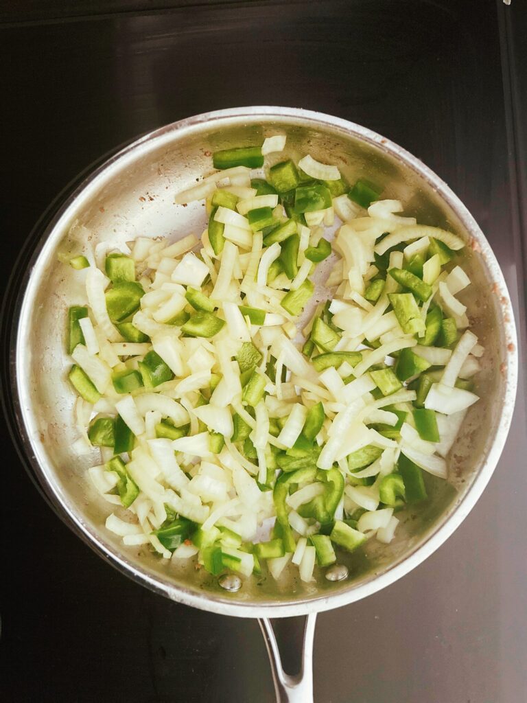 onion, green bell pepper, and garlic cooking in a frying pan