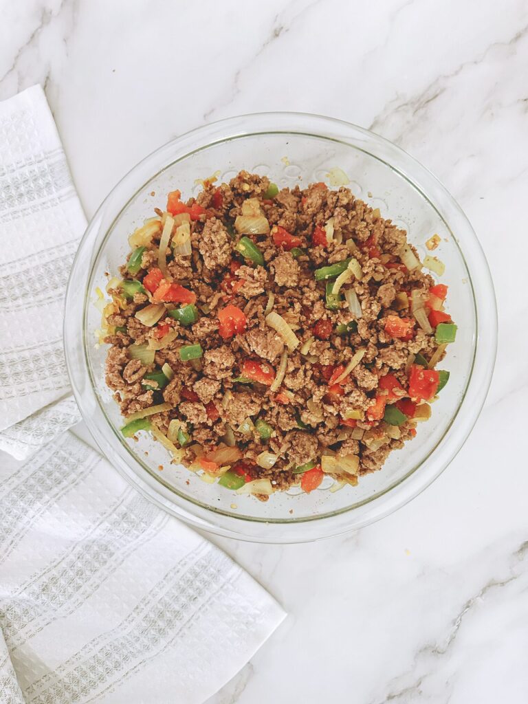 cooked ground beef, diced tomatoes, green bell pepper, onion, and garlic mixed together in a glass bowl