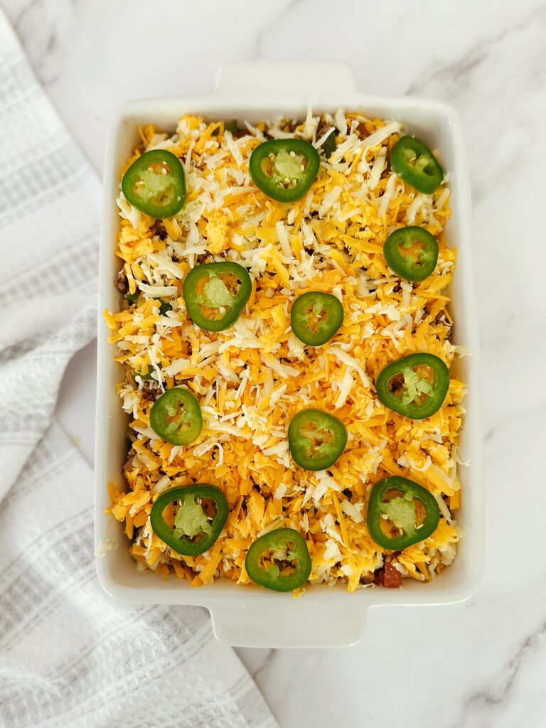 white porcelain casserole dish filled with keto mexican ground beef casserole mix topped with cheese and jalapeno slices