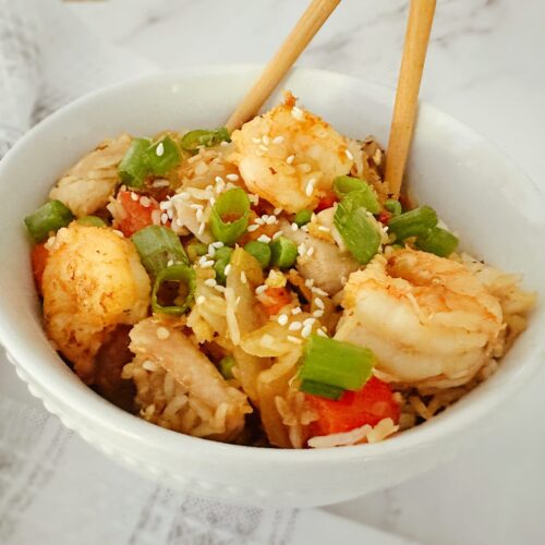 chinese chicken and shrimp stir fry in a white bowl with wooden chopsticks in the bowl and a kitchen rag in the background