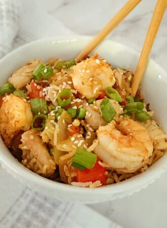 chinese chicken and shrimp stir fry in a white bowl with wooden chopsticks in the bowl and a kitchen rag in the background