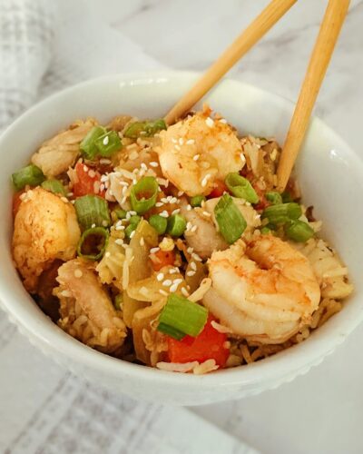 chinese chicken and shrimp stir fry in a white bowl with wooden chopsticks in the bowl and a kitchen rag in the background