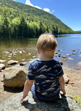 toddler facing a lake sitting on a rock