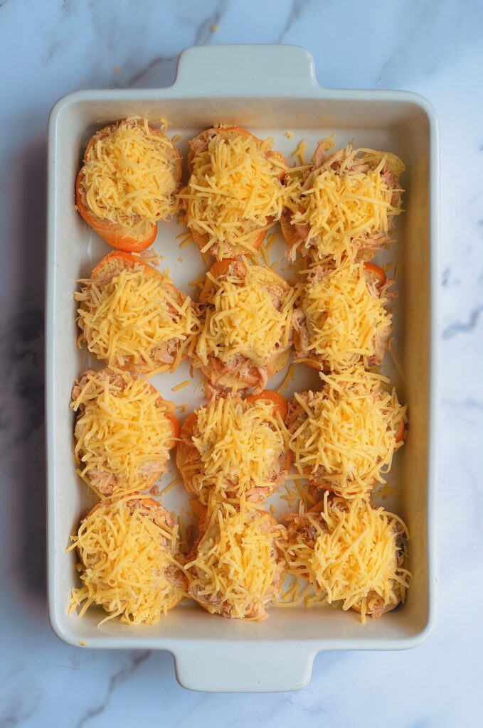 pulled chicken sliders with shredded cheese in a white dish