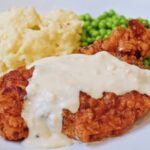 chicken fried chicken with country gravy on a plate with peas and mashed potatoes