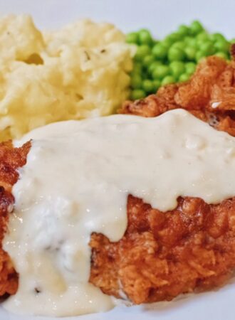 chicken fried chicken with country gravy on a plate with peas and mashed potatoes