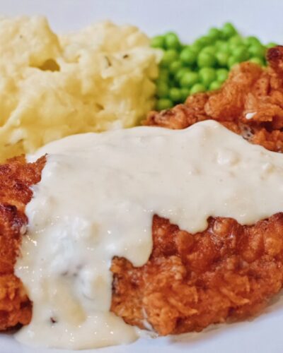 chicken fried chicken with country gravy on a plate with peas and mashed potatoes