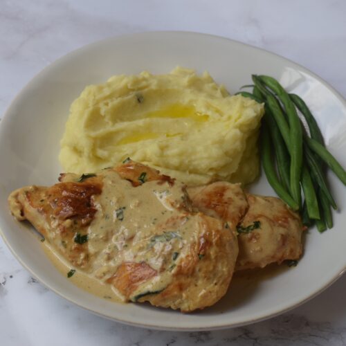 Boursin chicken on a white plate with mashed potatoes and green beans